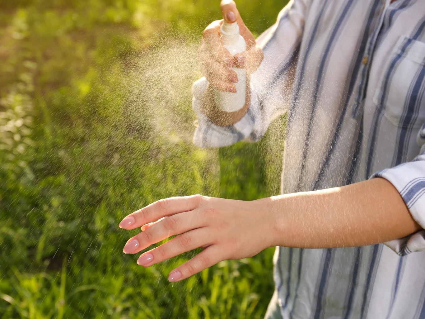 Jak zrobić domowy spray, który skutecznie odstraszy kleszcze? Osoba w koszuli z długim rękawem rozpyla domowy spray na rękę na tle zieleni w ogrodzie.