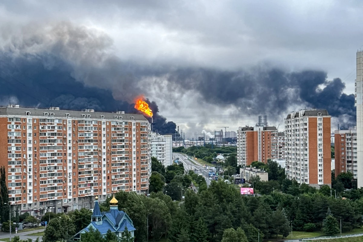 Ukraińskie drony uderzyły w czwartek w rafinerię ropy w Moskwie Rafineria ropy w Moskwie po ataku dronów, płomienie i czarny dym, w tle bloki oraz zieleń.
