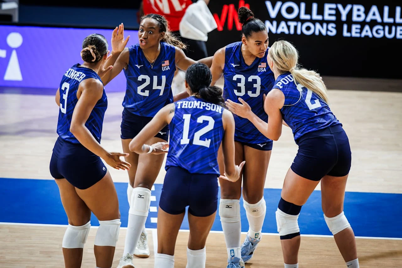 Siatkarki reprezentacji USA Zawodniczki amerykańskiej drużyny siatkówki w niebieskich strojach zbierają się w kole na boisku, przygotowane do kolejnej akcji podczas meczu.