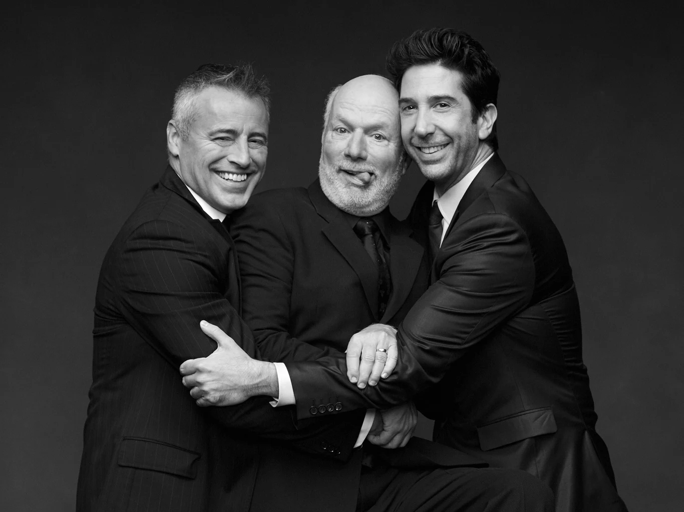 Matt LeBlanc, James Burrows i David Schwimmer w 2016 roku Trzech mężczyzn w garniturach obejmuje się nawzajem, dwaj z nich uśmiechają się szeroko, a środkowy wyciąga język, tworząc zabawną i luźną atmosferę.