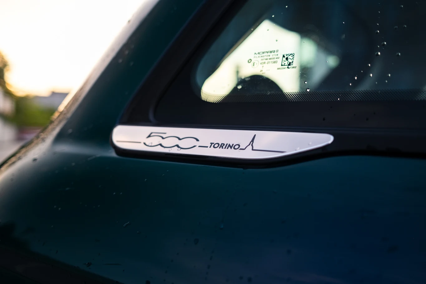 Emblemat z napisem '500 Torino' oraz stylizowaną linią na zielonym nadwoziu samochodu obok tylnej szyby.