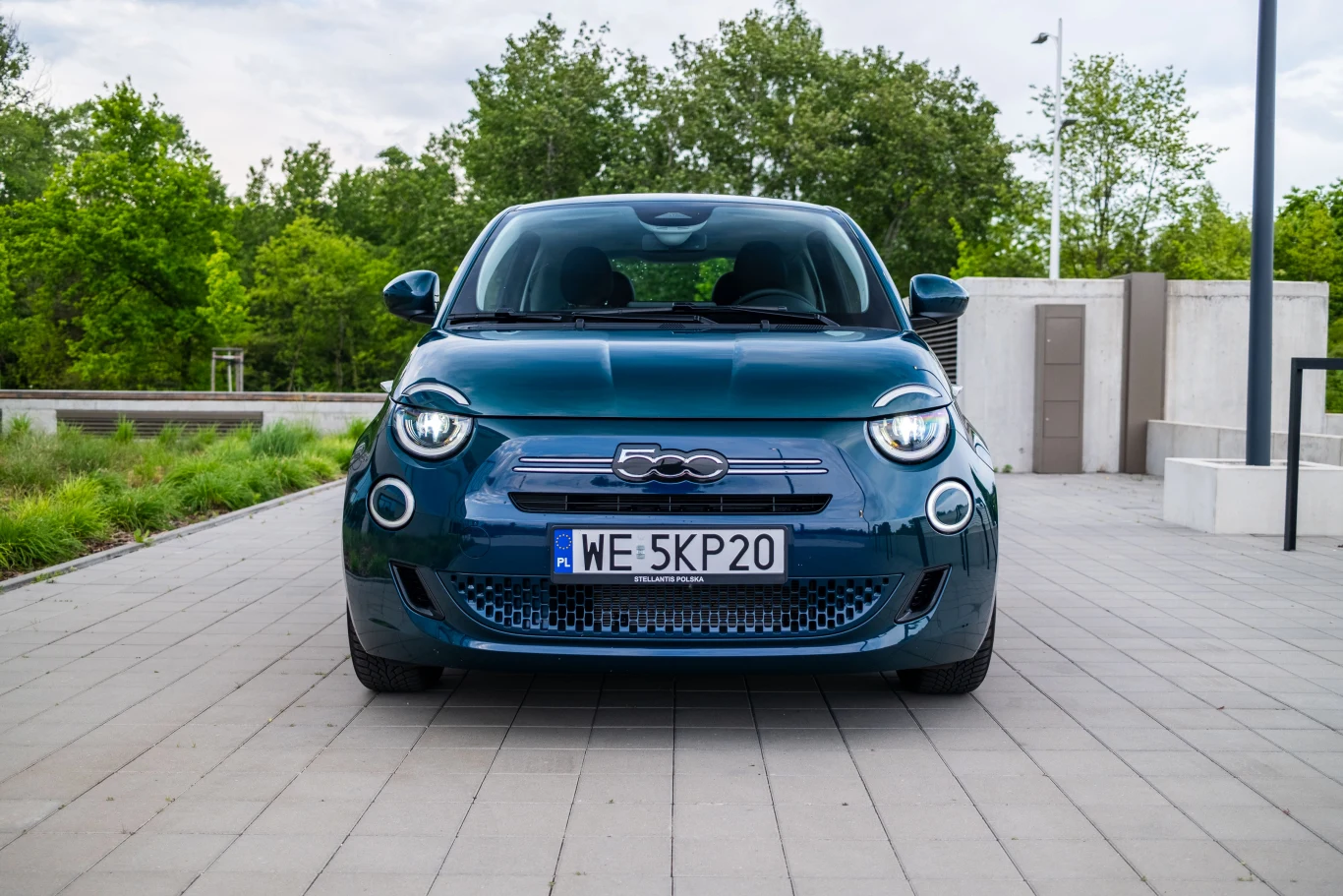 Nowoczesny, niebieski Fiat 500 zaparkowany przodem na chodniku, z widoczną rejestracją i charakterystycznym logo marki na grillu.
