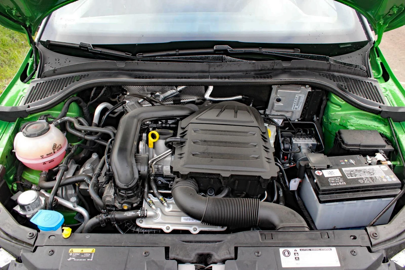 Skoda Fabia III 1.0 TSI Silnik samochodowy umieszczony centralnie, z widocznym akumulatorem po prawej stronie, zbiornikiem płynu chłodniczego po lewej oraz licznymi przewodami i elementami układu mechanicznego.