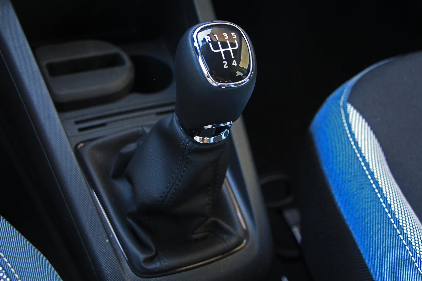 Skoda Fabia III Dźwignia manualnej skrzyni biegów z widocznym schematem przełożeń, otoczona czarną osłoną i fragmentem fotela z niebieskim obszyciem.