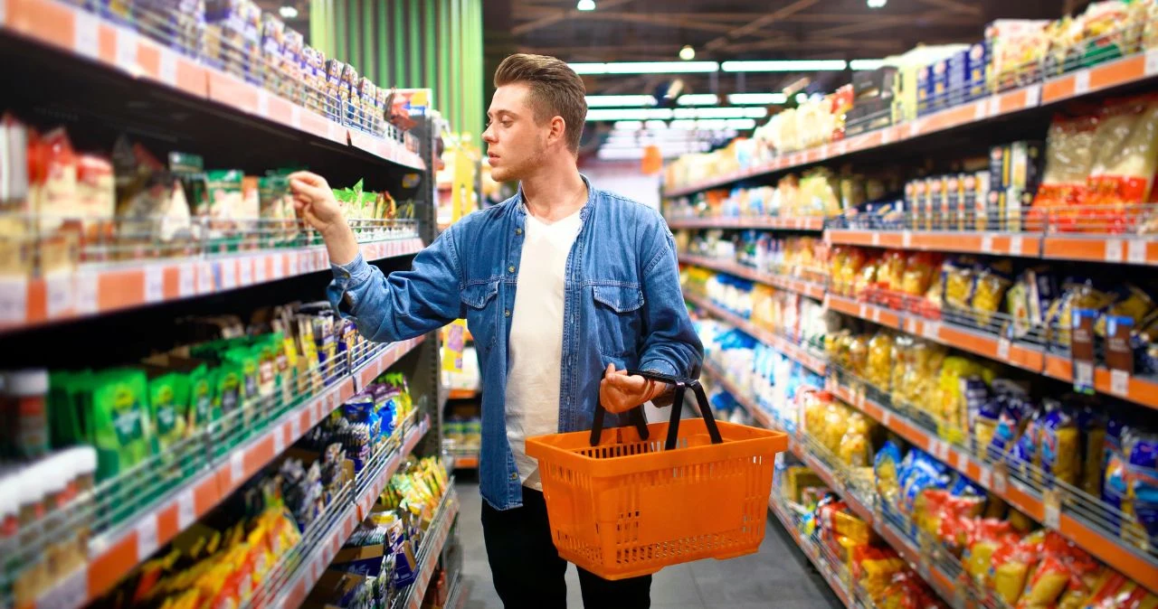 Kaufland ruszył z „Mocnym Startem”. Warzywa i kawy taniej o 76% tylko do środy Mężczyzna z pomarańczowym koszykiem wybiera produkty spożywcze przy regałach w sklepie Kaufland.