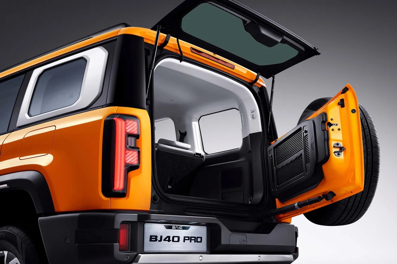 Otwarty bagażnik pomarańczowego SUV-a BJ40 PRO z unoszoną tylną szybą i rozchylonymi drzwiami, odsłaniający przestronne wnętrze pojazdu.