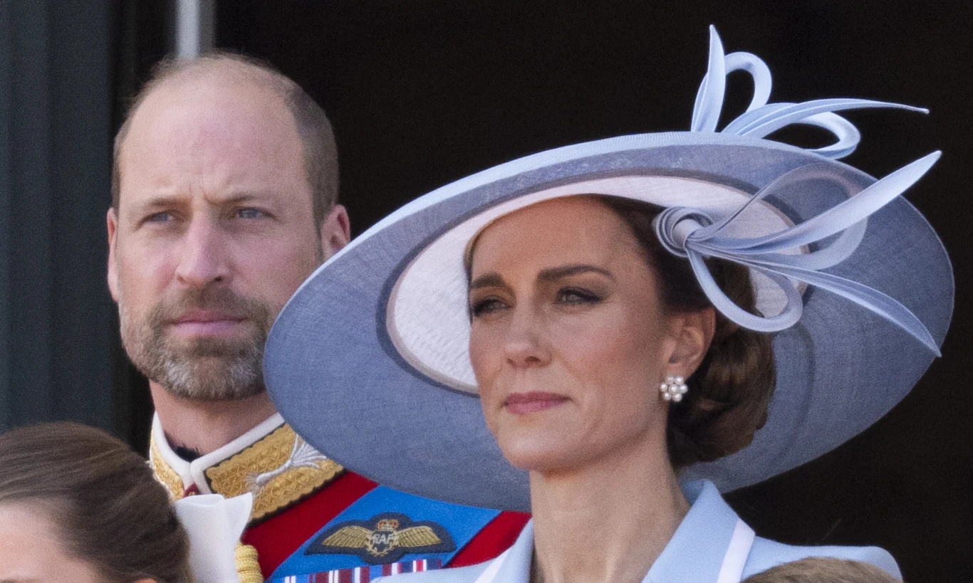 Elegancka kobieta w dużym, jasnoniebieskim kapeluszu z dekoracyjnymi elementami oraz mężczyzna w formalnym stroju z orderami i odznaczeniami, oboje stoją obok siebie, patrząc w jednym kierunku.