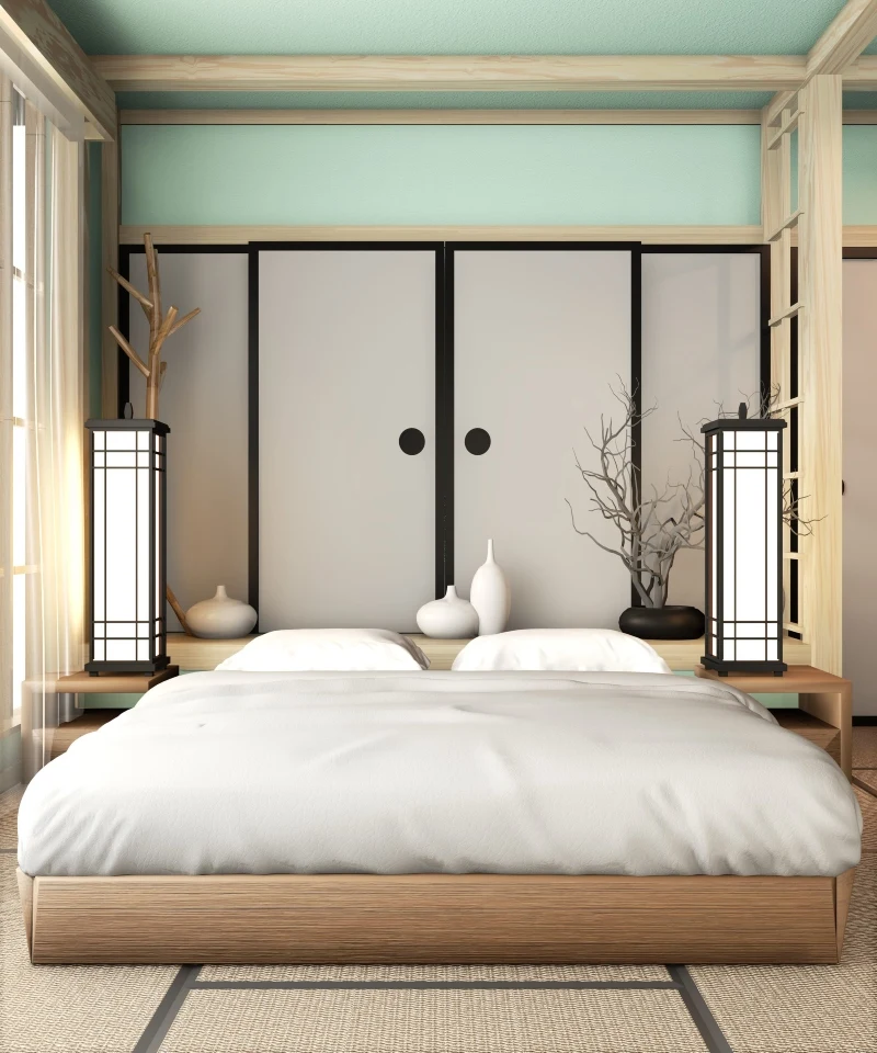 Hotelowy pokój w Japonii Minimalistyczne łóżko z jasną pościelą, dwa nowoczesne lampiony po bokach, dekoracyjne gałęzie oraz białe ceramiczne wazony ustawione na niskich szafkach przy przesuwanych drzwiach w stylu japońskim.