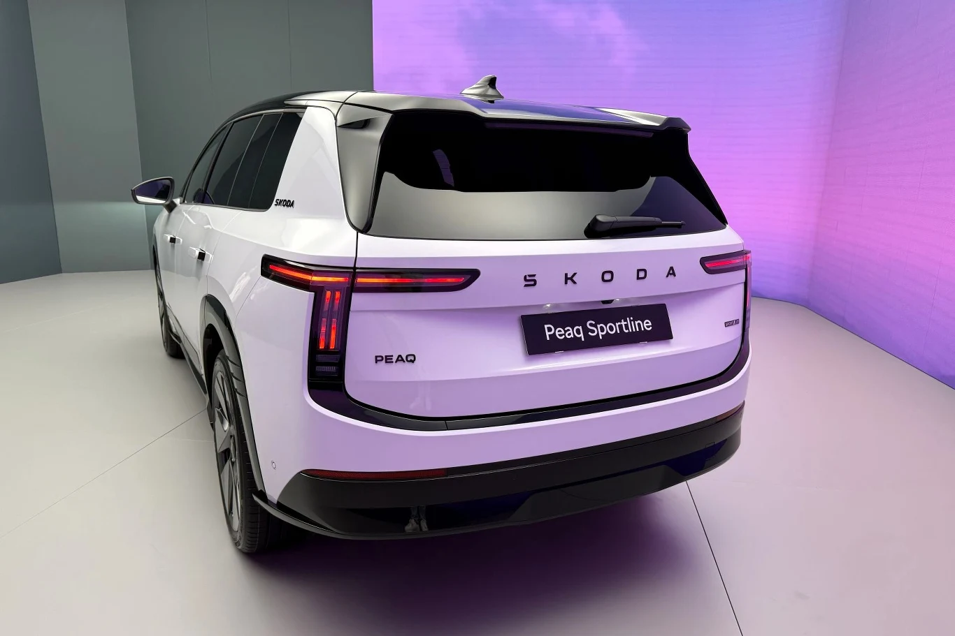 Biały SUV Škoda Peaq Sportline z nowoczesnym, czarnym wykończeniem dachu i smukłymi, poziomymi światłami LED, prezentowany w jasnym, minimalistycznym wnętrzu.