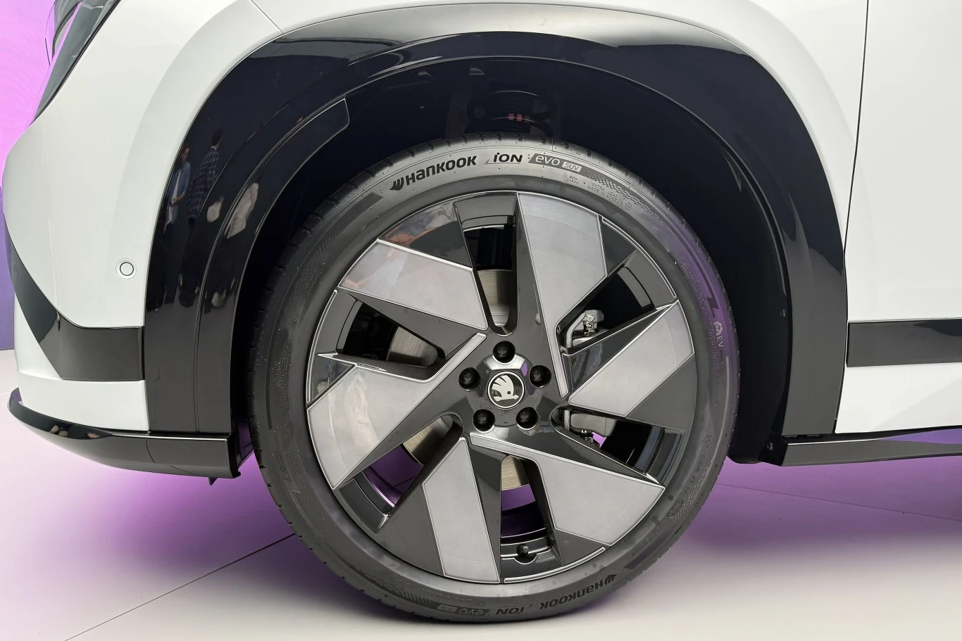 Duża felga aluminiowa z wyrazistymi, geometrycznymi ramionami, opona Hankook oraz fragment białego nadwozia samochodu z czarnym nadkolem.