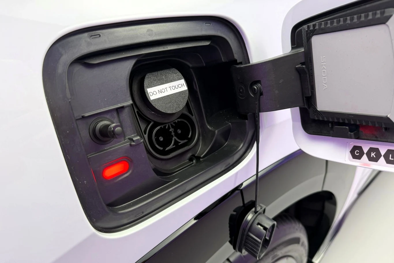 Gniazdo ładowania samochodu elektrycznego z otwartą klapką, widocznym wskaźnikiem świetlnym i zabezpieczonym złączem do ładowania.