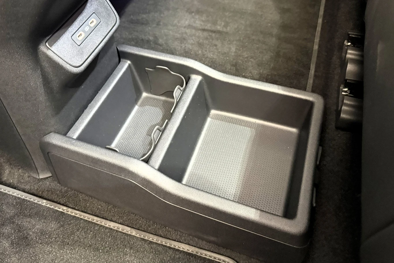 Plastikowy organizer na podłodze samochodu z podziałem na dwie przegródki oraz zintegrowanymi uchwytami na napoje.