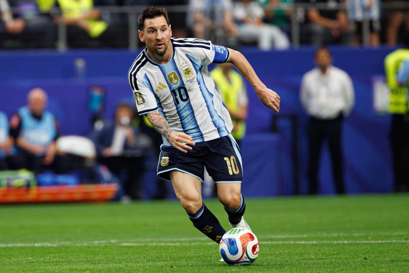 Lionel Messi Lionel Messi w biało-błękitnej koszulce z numerem 10 prowadzi piłkę podczas meczu piłkarskiego.