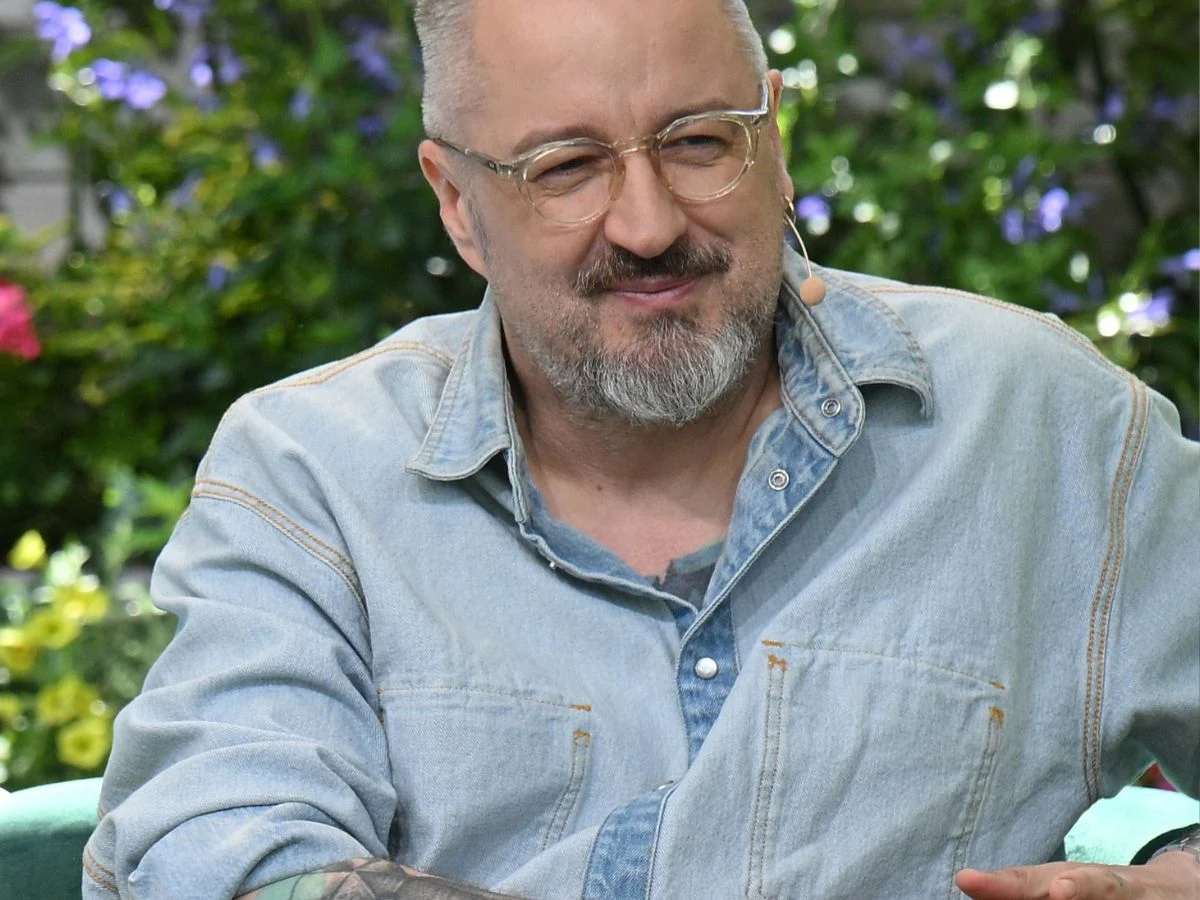 Piotr Kędzierski Piotr Kędzierski w jasnej jeansowej koszuli i okularach siedzący w ogrodzie.