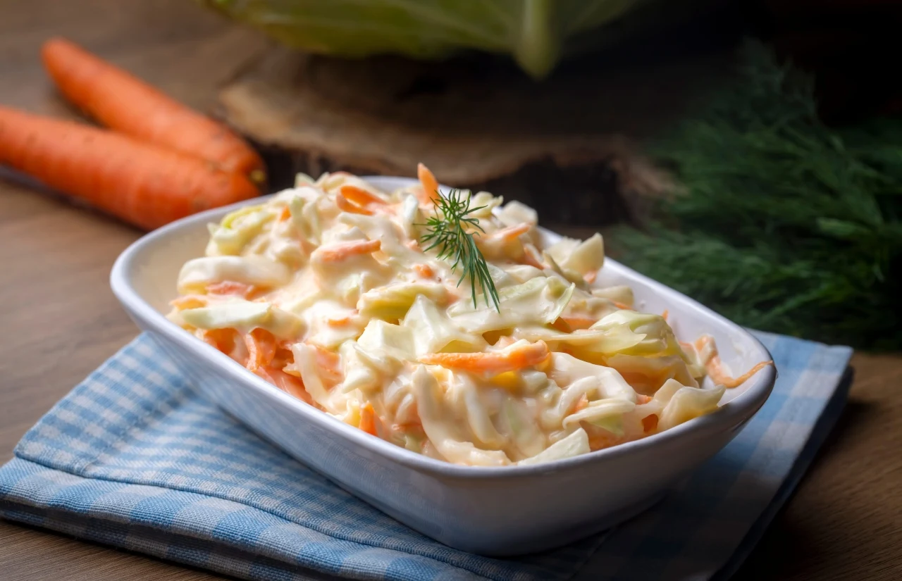 Surówka coleslaw, czyli spolszczony colesław Sałatka coleslaw z białą kapustą, marchewką i koperkiem w białej misce na lnianej ściereczce.