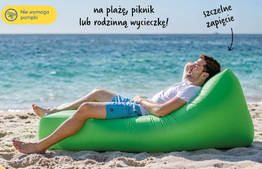 Mężczyzna w jasnej koszulce i niebieskich szortach odpoczywa na dmuchanym, zielonym leżaku na piaszczystej plaży z widokiem na morze; leżak wyróżnia się szczelnym zapięciem i nie wymaga użycia pompki.