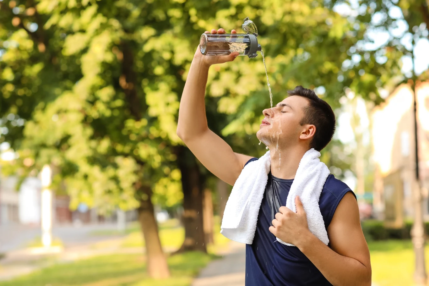 Jak trenować w upał bez ryzyka? Kilka prostych zasad Mężczyzna w sportowej koszulce polewa twarz wodą podczas przerwy w treningu na świeżym powietrzu w upale.