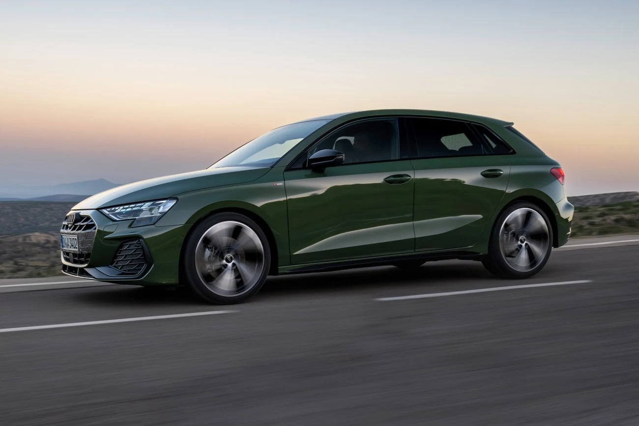 Zielone Audi A3 Sportback porusza się dynamicznie po asfaltowej drodze, na tle delikatnie rozjaśniającego się nieba o zmierzchu.
