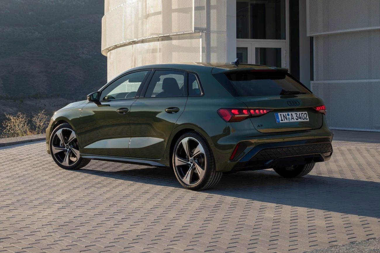 Zielony hatchback Audi A3 zaparkowany na utwardzonej nawierzchni przy nowoczesnym budynku, z widocznymi charakterystycznymi tylnymi lampami LED i dużymi felgami.