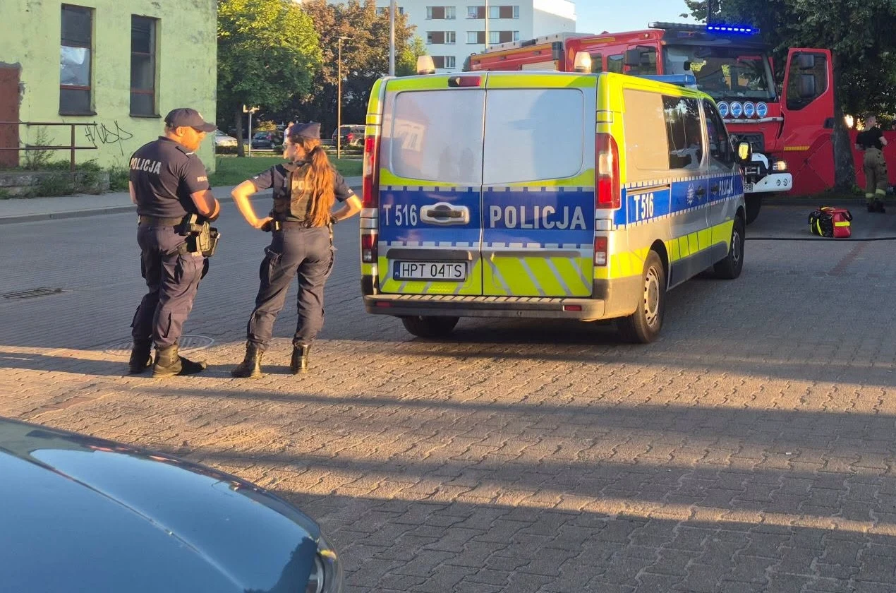 Ewakuacja komendy w Iławie Dwóch policjantów przy radiowozie z napisem 'Policja', w tle wóz strażacki z włączonymi światłami.