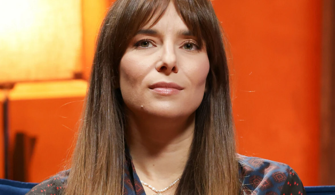 Anna Czartoryska-Niemczyka Anna Czartoryska-Niemczycka w granatowej bluzce i naszyjniku z pereł na tle pomarańczowej ściany.