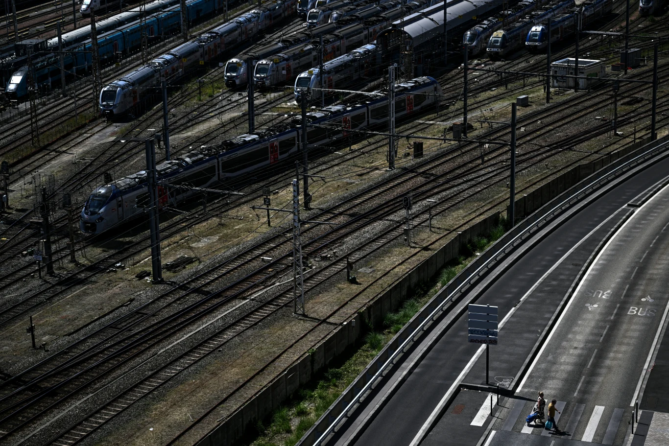 Z powodu upałów w Europie wstrzymywane są pociągi. Wysokie temperatury grożą uszkodzeniem torów Szereg stojących pociągów na wielotorowej stacji kolejowej, obok trójka ludzi przechodzi przez przejście.