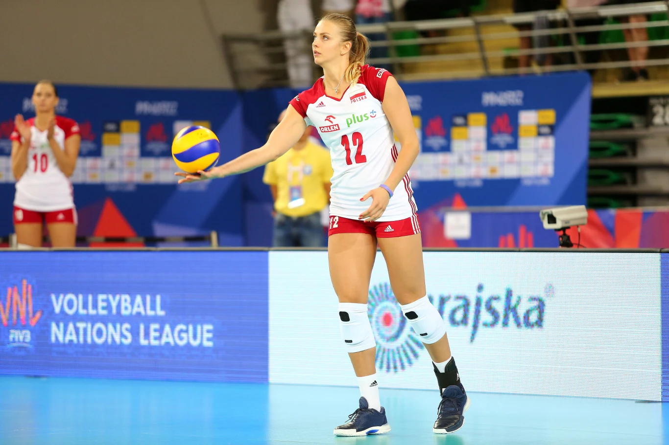 Natalia Murek Siatkarka reprezentacji Polski przygotowująca się do wykonania zagrywki podczas meczu, trzyma piłkę w jednej ręce i koncentruje się na grze.