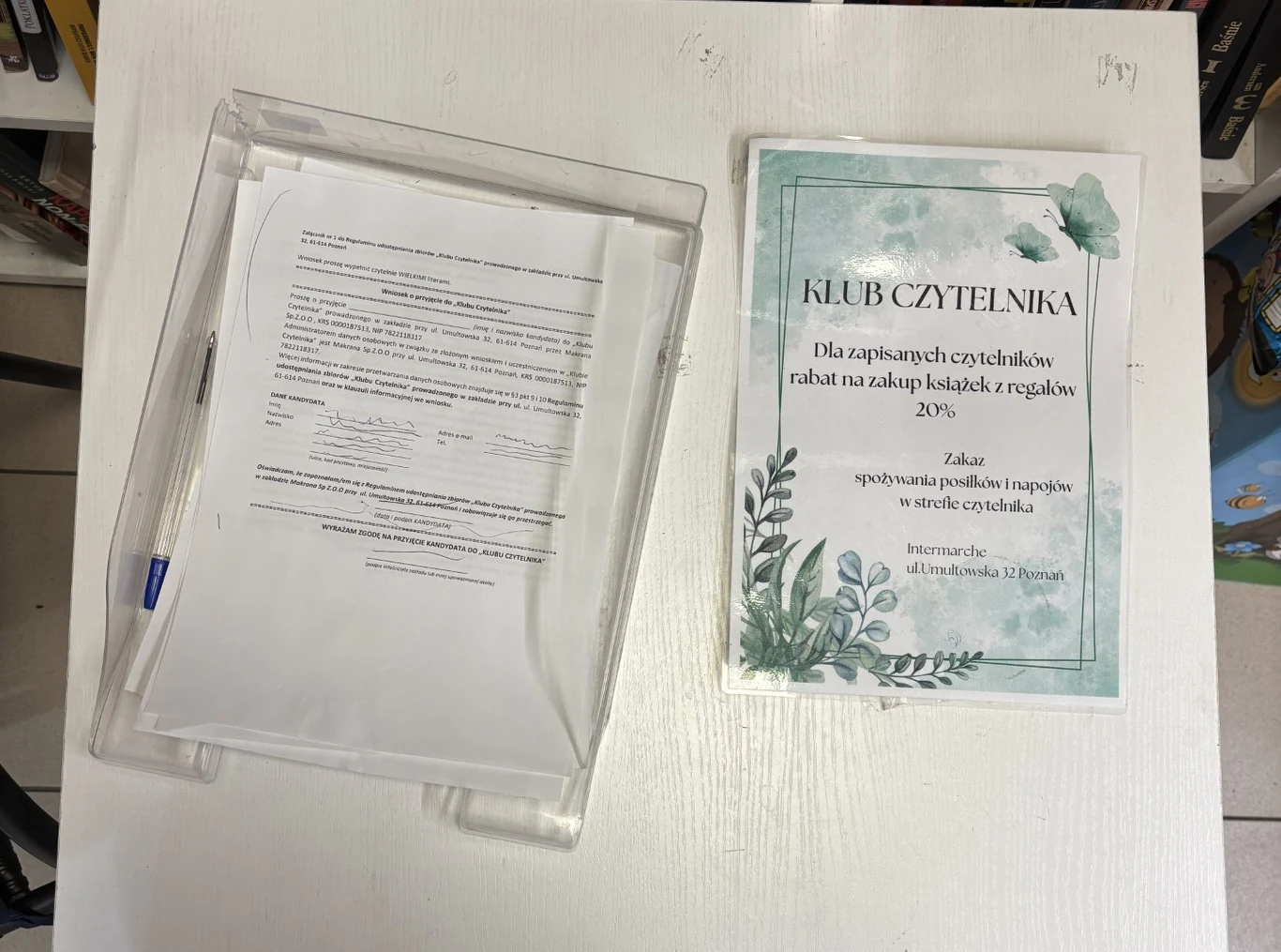 Przezroczysta tacka z wydrukowanymi dokumentami oraz informacja o Klubie Czytelnika z ofertą rabatu na zakupy książek i szczegółami dotyczącymi zapisu.