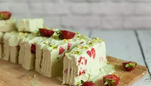 Pistachio ice cream with strawberry and pistachio nuts on a light wooden background