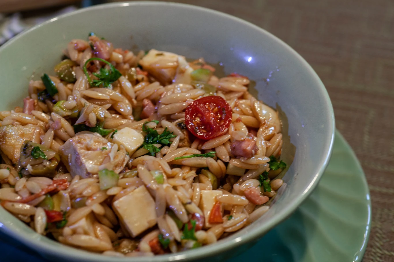 Do sałatki z makaronem orzo można dodawać dowolne warzywa i modyfikować przepis wedle uznania. Świetnie sprawdzą się także pomidorki koktajlowe Sałatka z makaronem orzo, kostkami sera, kawałkami pomidorów, świeżą natką pietruszki oraz kawałkami wędliny, podana w głębokiej misce.