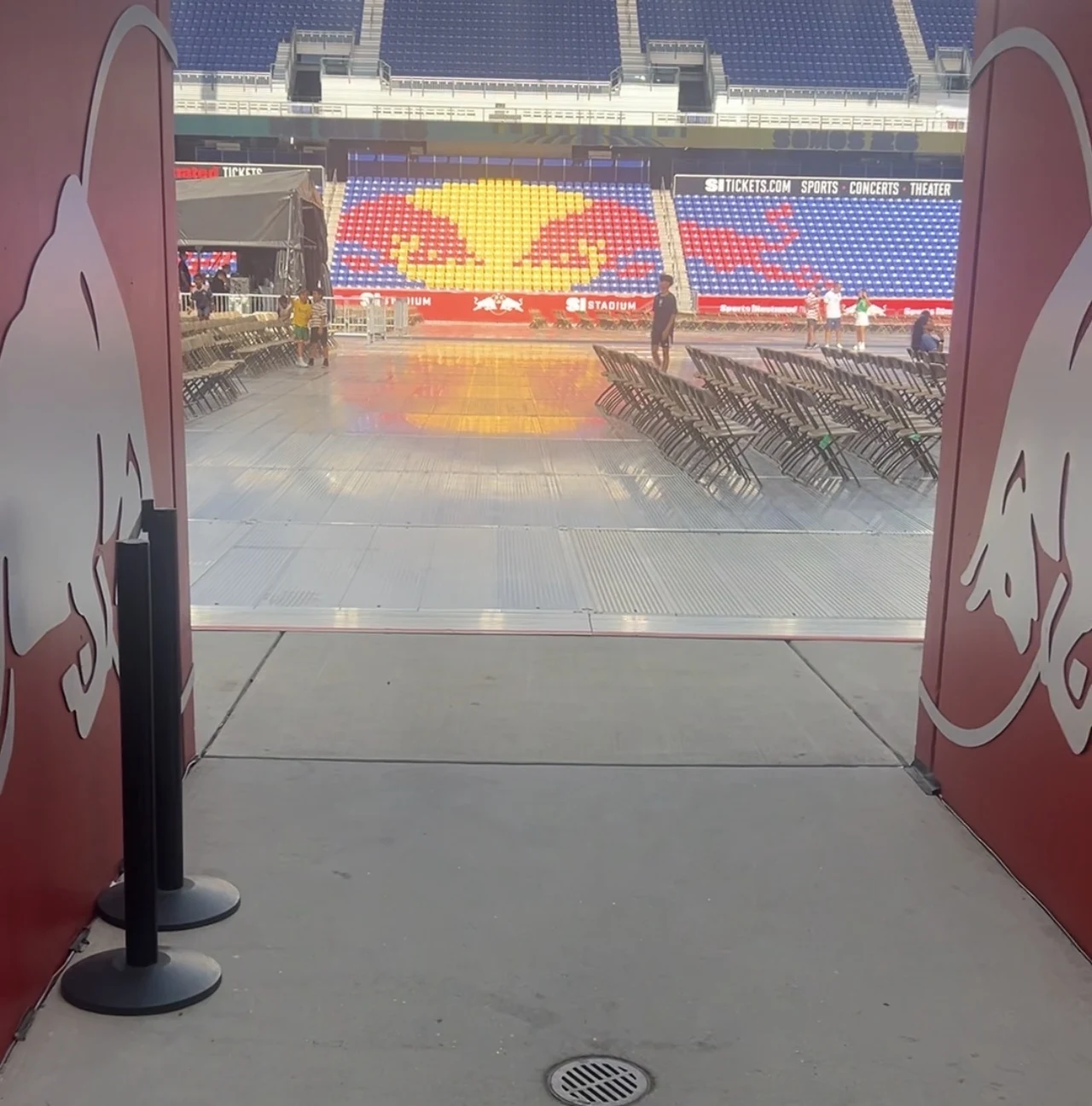 Taki widok oglądają piłkarze New York Red Bulls wychodząc z tunelu Wejście na stadion prowadzące na główną płytę, w tle rzędy ułożonych krzeseł oraz duża mozaika w barwach klubu z żółto-czerwonym logo byka na trybunach.