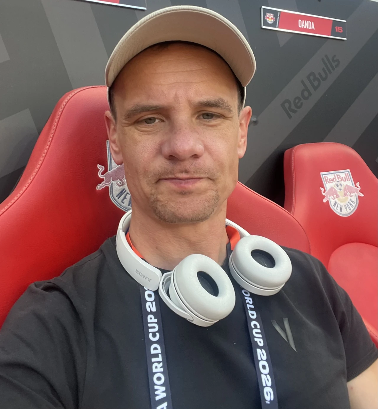 Ławki rezerwowych mieszczą się w pierwszym rzędzie trybun - przy sektorze VIP. Są bardzo wygodne Mężczyzna w jasnej czapce z daszkiem i słuchawkami na szyi siedzi na czerwonym fotelu z logo Red Bull oraz napisem WORLD CUP 2026 na smyczy.