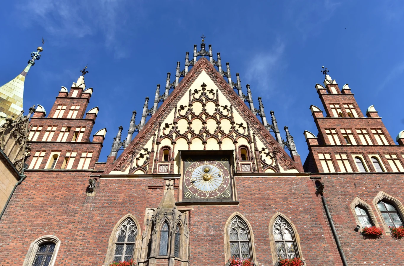 Wrocławski ratusz i rynek to dopiero początek zwiedzania miasta Wrocławski ratusz na rynku, gotycka fasada z wysokim szczytem, zegarem i witrażowymi oknami z kwiatami.
