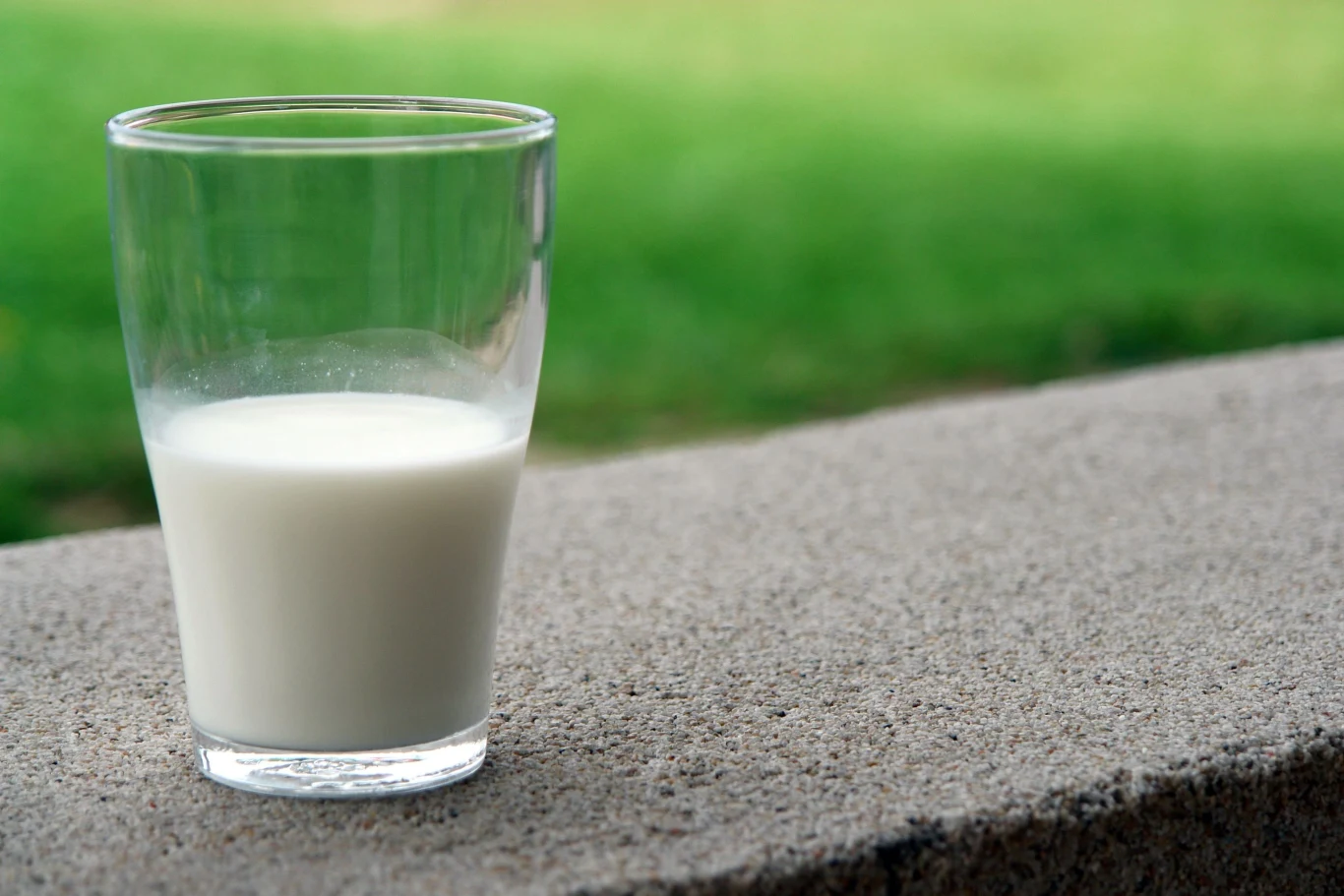Kefir zadziała chłodząco i łagodząco na oparzenia słoneczne Szklanka z kefirem stojąca na betonowej powierzchni; w tle widoczna zieleń.