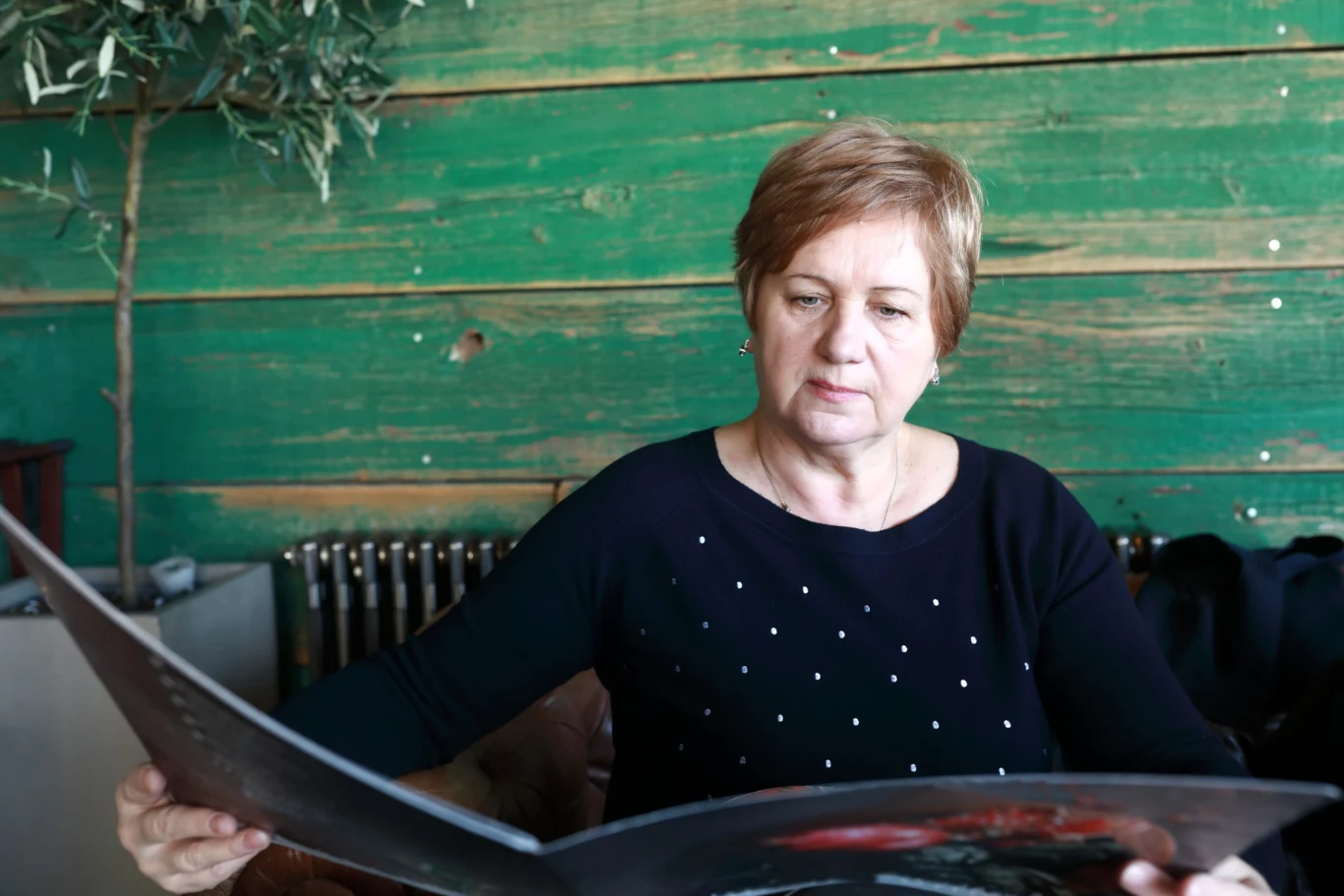 Zdarza się, że dorośli wolą zamówić danie z menu dziecięcego. Czy kelner może odmówić? Kobieta w średnim wieku uważnie przegląda duży arkusz papieru, siedząc przy zielonej, drewnianej ścianie.