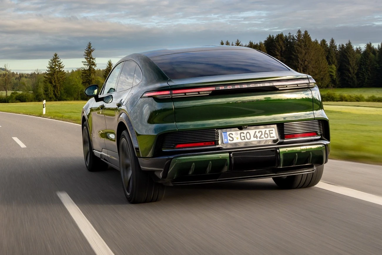 Zielone sportowe auto Porsche Taycan podczas jazdy po asfaltowej drodze, otoczonej przez zielone pola oraz lasy.