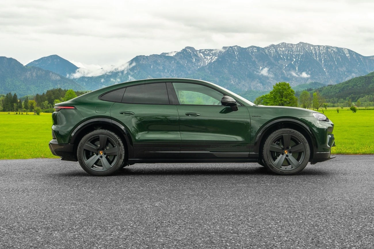 Zielony SUV o sportowej sylwetce zaparkowany na asfalcie, w tle zielone łąki i góry z ośnieżonymi szczytami.