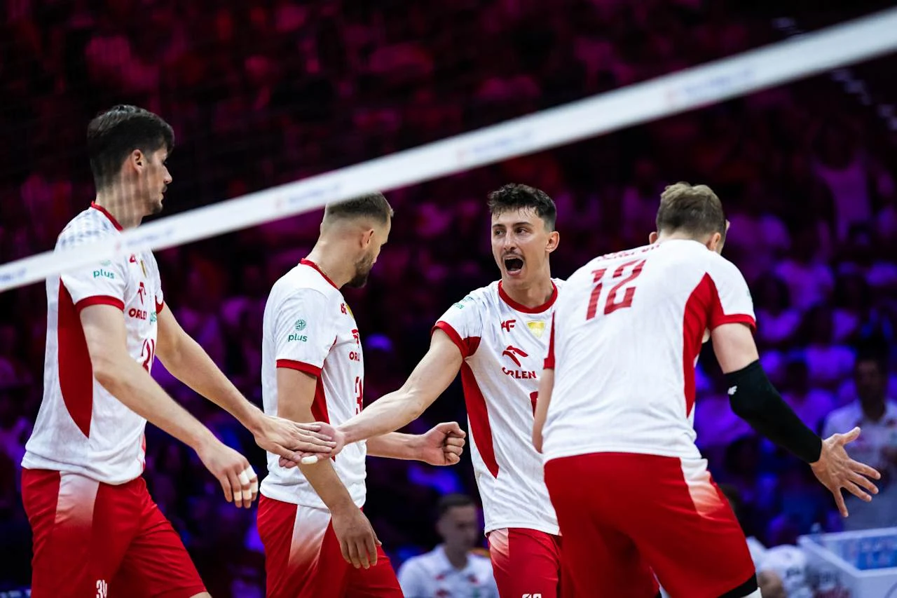 Grupa siatkarzy ubranych w biało-czerwone stroje, świętujących udaną akcję na boisku podczas meczu, z wyraźnymi emocjami i gestami triumfu.