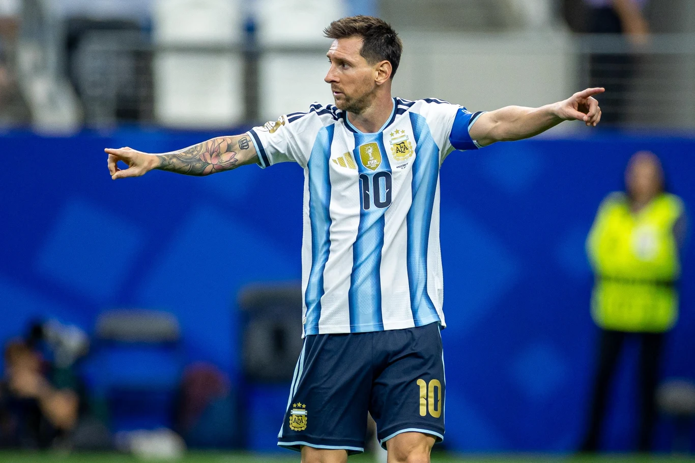 Leo Messi Piłkarz w koszulce reprezentacji Argentyny z numerem 10 stoi na murawie, gestykulując obiema rękami w kierunku różnych stron boiska.