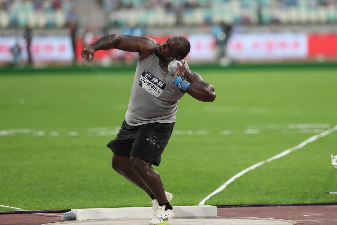 Rajindra Campbell Zawodnik w trakcie pchnięcia kulą na stadionie lekkoatletycznym, skupiony na technice rzutu, ubrany w sportowy strój z numerem startowym.
