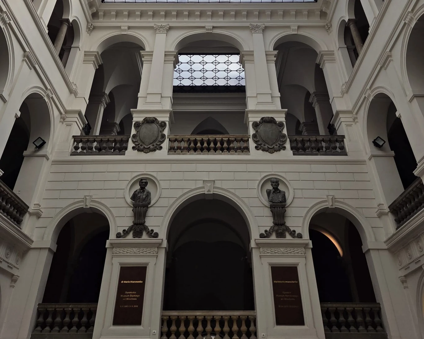 Imponujące wnętrze budynku z trzema kondygnacjami arkad, dwoma rzeźbami postaci w niszach oraz dekoracyjnymi balustradami i detalami architektonicznymi w stylu klasycystycznym.