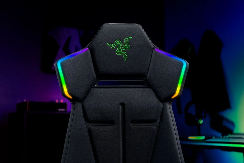 Czarny fotel gamingowy z podświetleniem LED na oparciu oraz zielonym logo Razer pośrodku zagłówka.