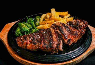 Grillowana karkówka podana z frytkami i zielonymi papryczkami na żeliwnej patelni 