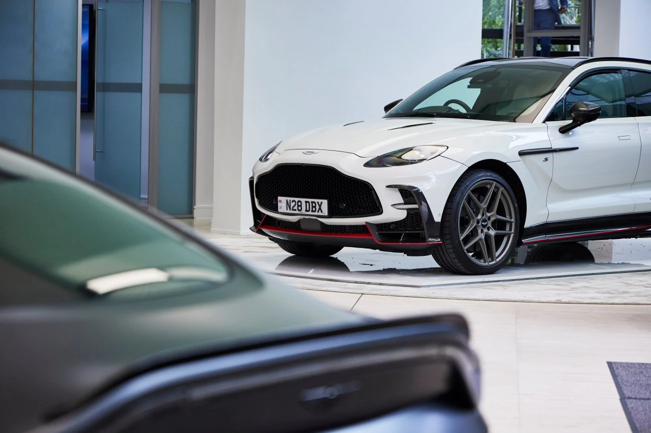 Biały sportowy samochód Aston Martin z czarnymi elementami i czerwonym akcentem na zderzaku stoi w nowoczesnym salonie.