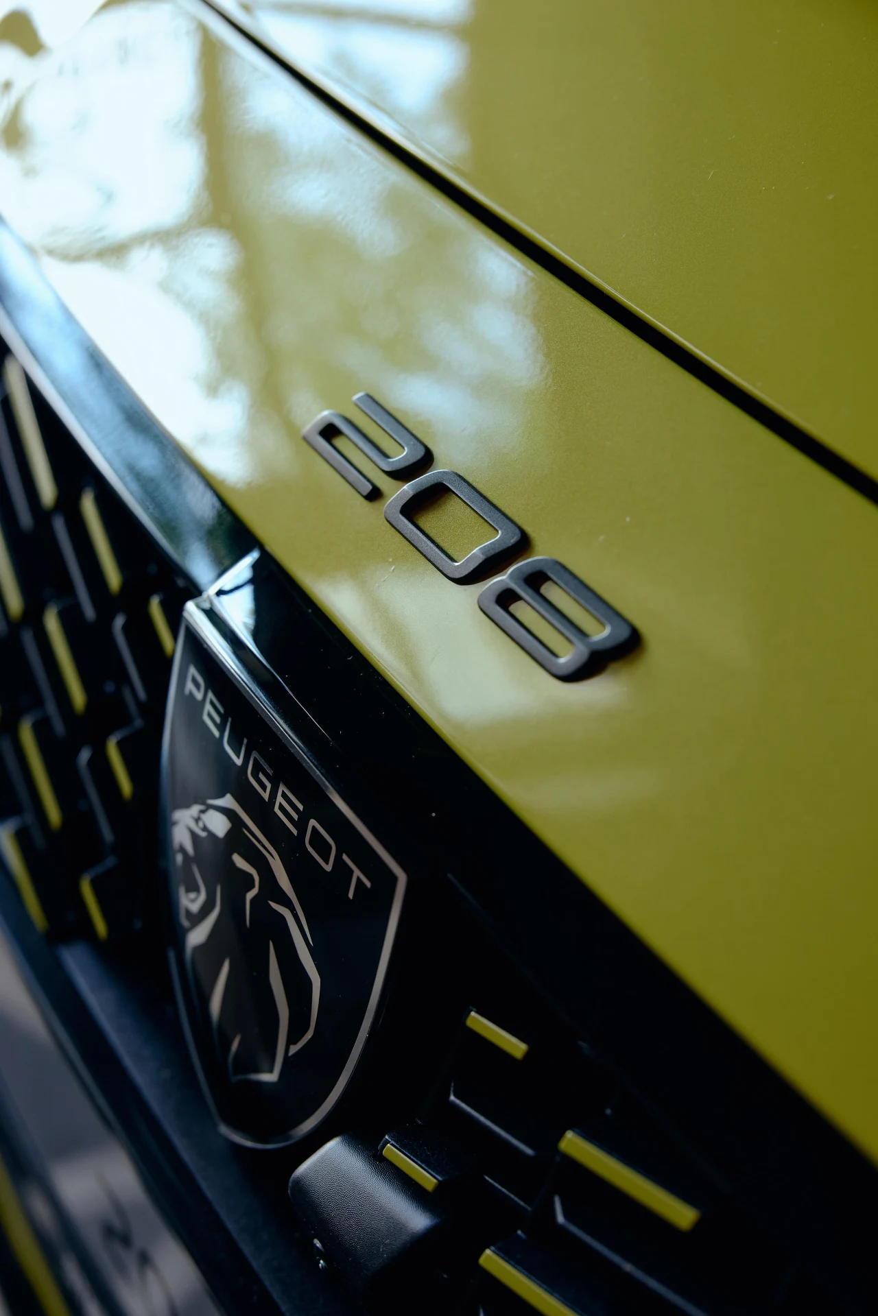 Zbliżenie na przednią maskę żółtego Peugeota 208 z widocznym logo marki oraz napisem modelu.