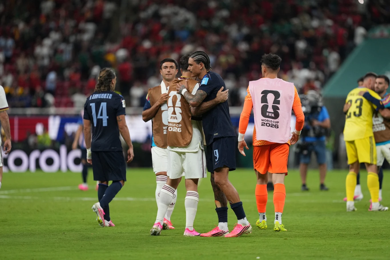 Urugwaj - Hiszpania Dwóch piłkarzy Urugwaju i Hiszpanii obejmuje się na środku boiska po meczu, wokół inni zawodnicy i sztab z kamizelkami FIFA 2026.