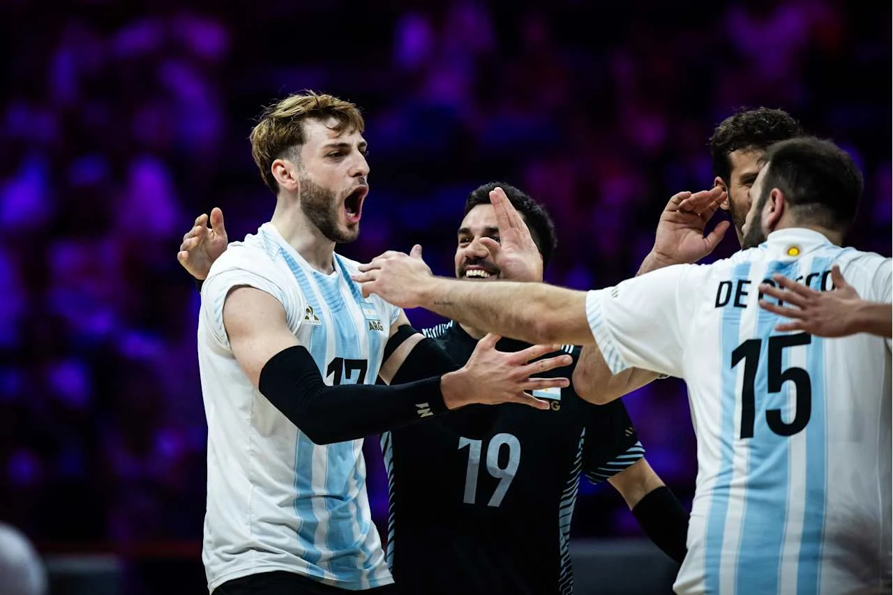 Zawodnicy argentyńskiej drużyny siatkarskiej w białych i niebieskich strojach świętują zdobycie punktu, okazując radość i energię na boisku.