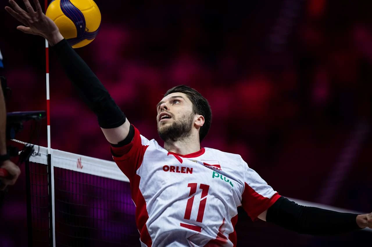 Aleksander Śliwka w trakcie meczu z Argentyną Siatkarz w biało-czerwonym stroju z numerem 11 wykonuje atak, sięgając piłki tuż przy siatce podczas meczu siatkówki.