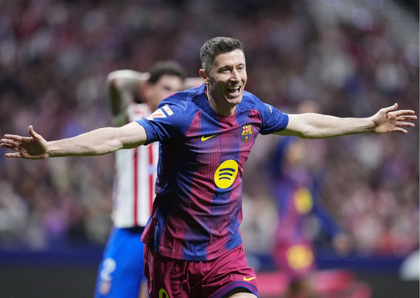 Piłkarz Barcelony w bordowo-granatowej koszulce z charakterystycznym logotypem Spotify świętuje zdobycie bramki z szeroko rozłożonymi ramionami na tle rozmytej publiczności stadionu.