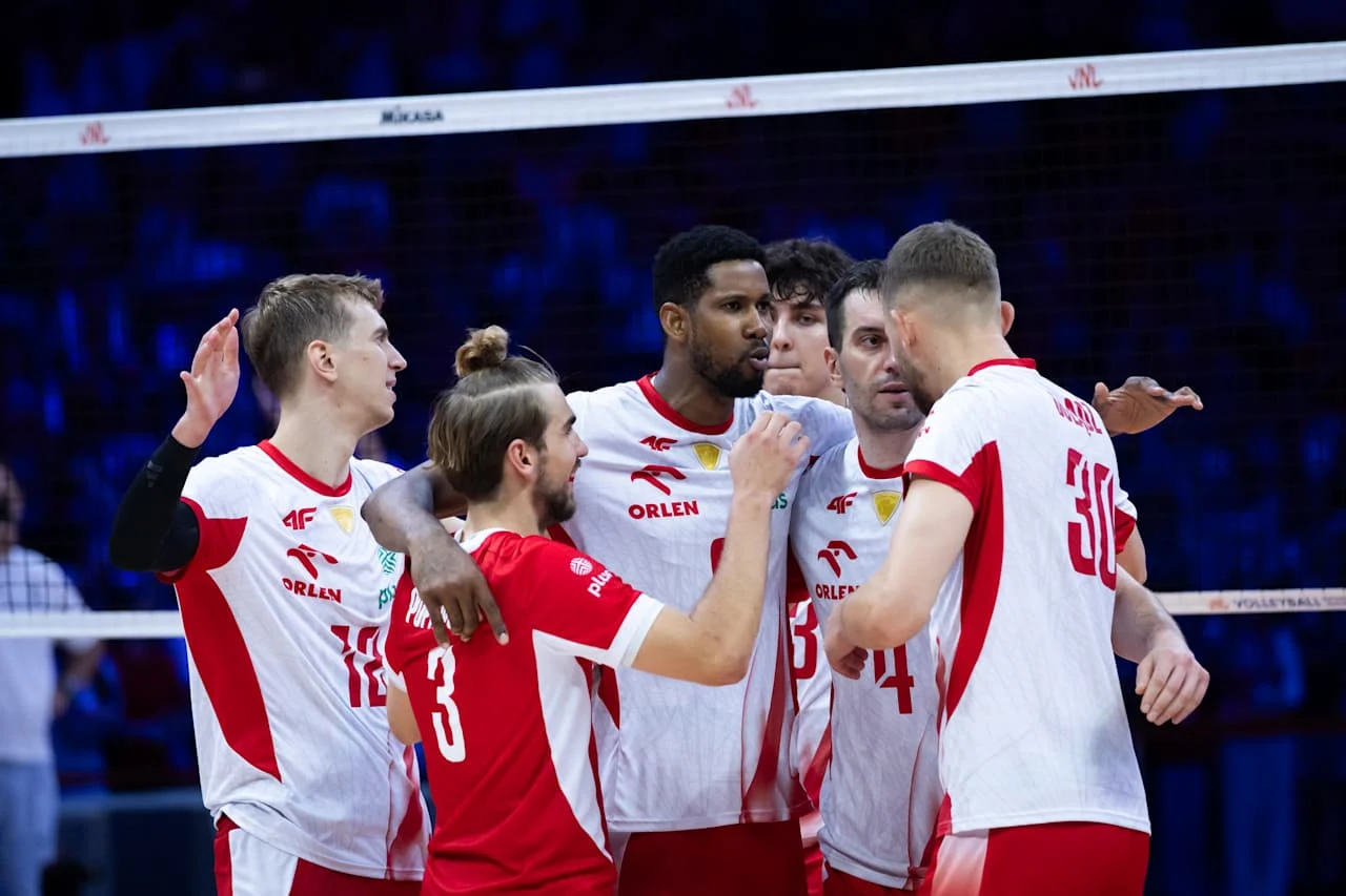 Wilfredo Leon w otoczeniu kolegów z reprezentacji Polski Grupa polskich siatkarzy w białych i czerwonych strojach świętuje razem punkt podczas meczu, unosząc ręce i okazując radość.